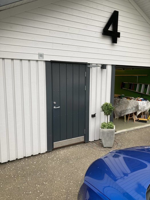 Renoverad garagedörr i mörkgrå med nytt handtag, gångjärn och sparkplåt på en vitmålad vägg.