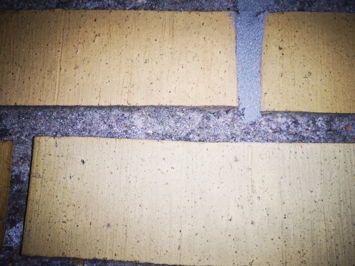 Närbild på en del av en gul tegelvägg som visar sliten och delvis skadad fog mellan tegelstenarna.