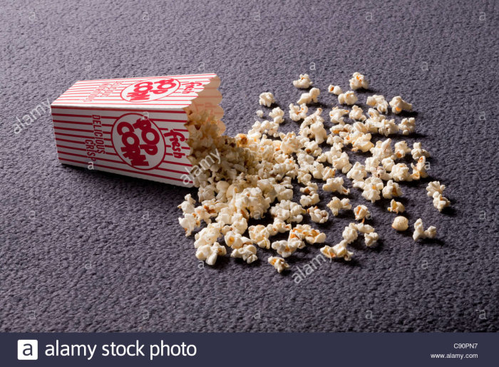 Vält popcornförpackning med popcorn utspridda på en mörkgrå matta.