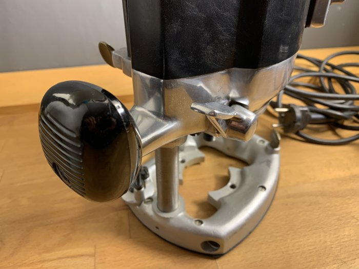 Välbevarad överfräs med skärphuvud, spänd knopp och elsladd på ett arbetsbord.