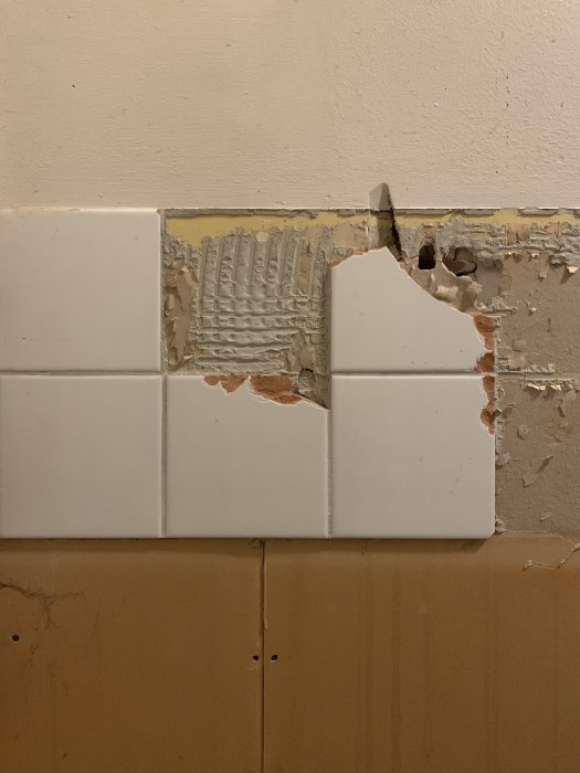Kakel på vägg med skadad gipsvägg där delar av kaklet och väggen är avlägsnade.