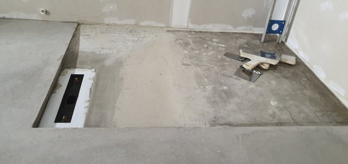 Nyggjutet betonggolv i rum, med markerat lokalfall och verktyg, plats för framtida duschvägg synlig.