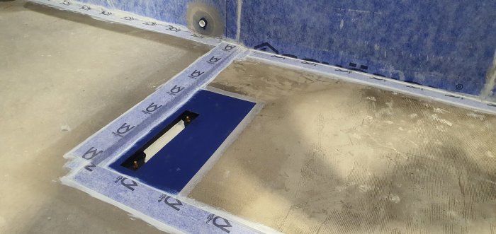 Golv i renoveringsprocess med Dallmer Tistoline brunn och blått tätskikt vid kakellist.