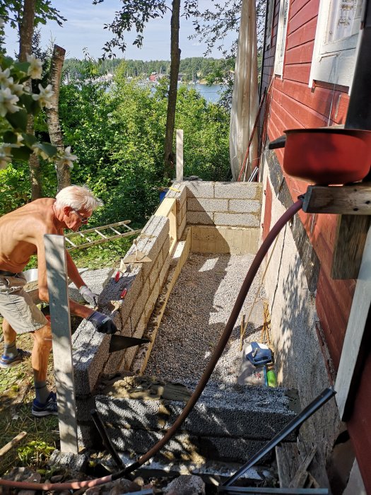 Man lägger lecablock för kökstillbyggnad vid stuga med sjöutsikt, sommar.