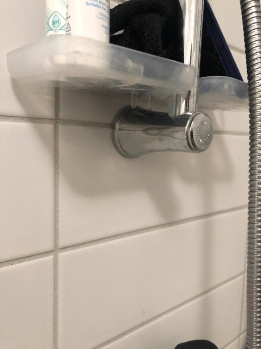 Duschhållare skruvad i kakelvägg med duschslang, en vit tvålkopp ovanpå, befintliga VVS-installationer i en modern lägenhet.
