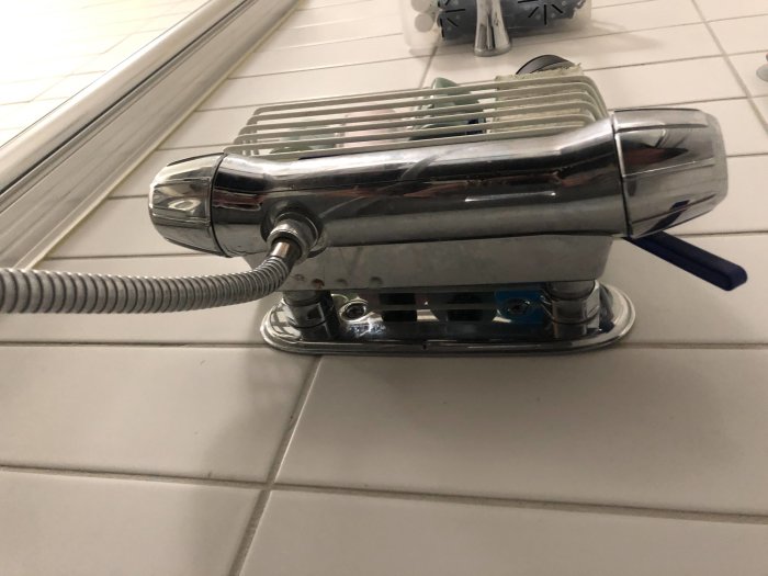 Kromad duschblandare med blå detaljer monterad på vitt kakel med duschslang ansluten.