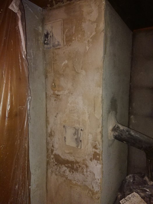 Delvis putsad murstock med sotlucka och plastövertäckt sidovägg under renovering.