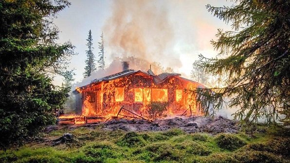 Fritidshus i lågor omgivet av träd i Jämtlandsfjällen, dokumenterat av räddningstjänsten.