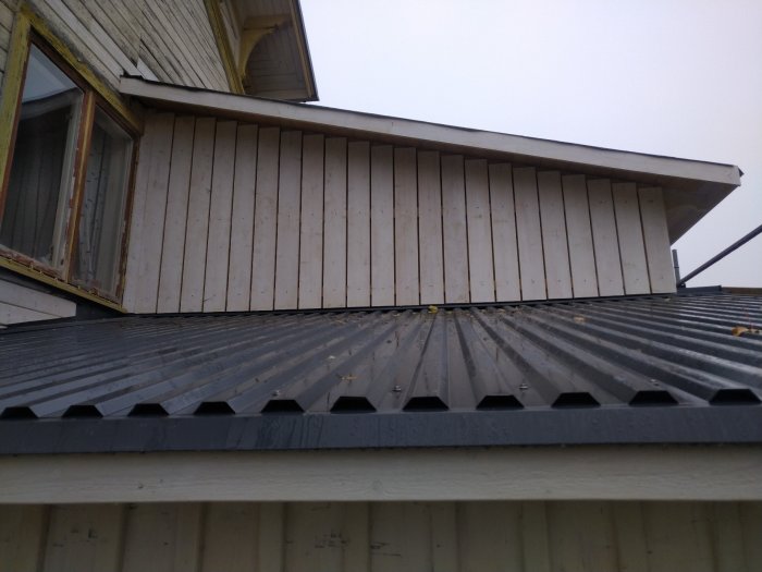 Ny spikad träpanel på en husväggs övre del över ett plåttak.