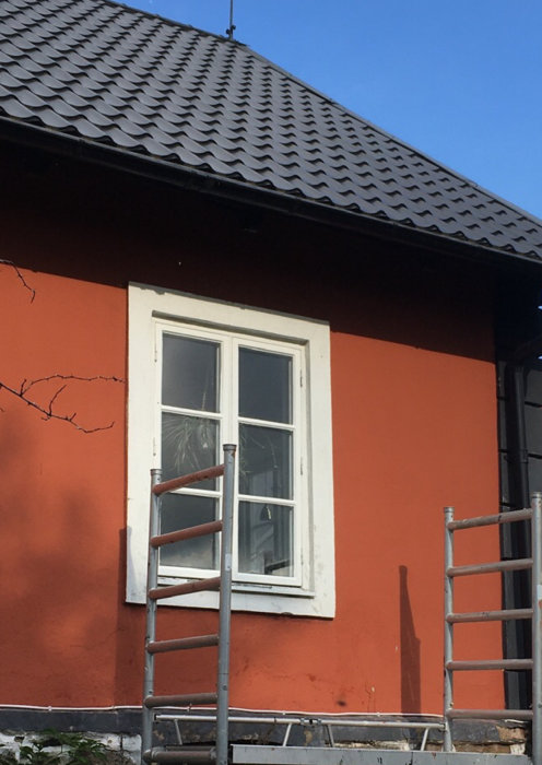 Nymålat fönster med linoljefärg på orange husfasad med byggställning framför.