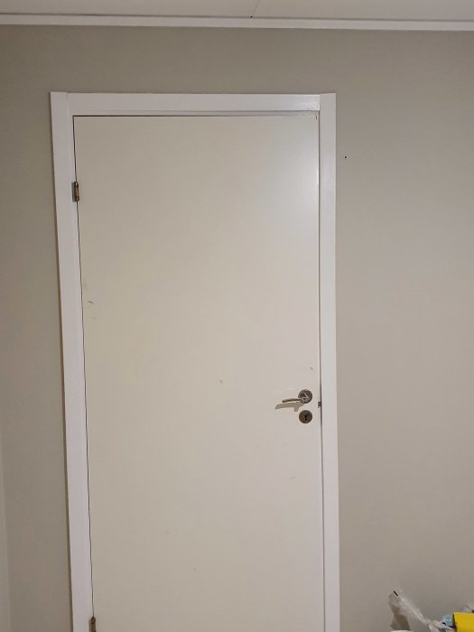 Vitmålad dörr med dörrfoder och taklist i vitt mot en ljus vägg.