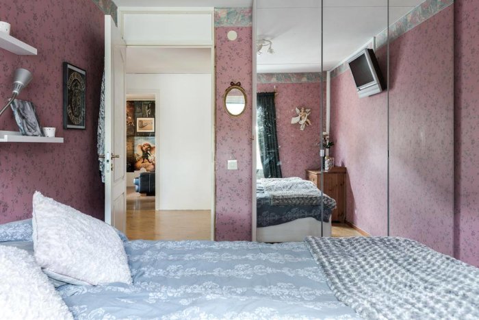 Sovrum i radhus före renovering med rosa blommig tapet, spegelgarderob och synlig säng.