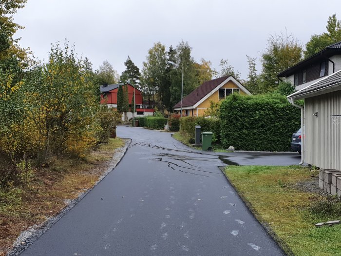 Ny asfalterad gata som lutar mot en garageuppfart med vattenspår som visar avrinningen.