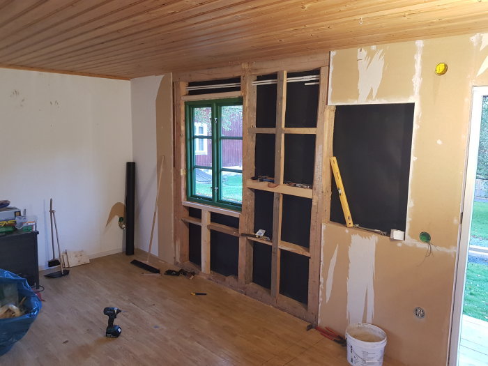 Nyinstallerat fönster i en pågående renoverad interiör med isolerade väggar och träpanel i taket.