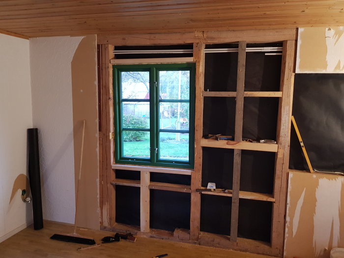 Nyinstallerat fönster i en vägg under renovering med synlig träregelstomme och verktyg på golvet.