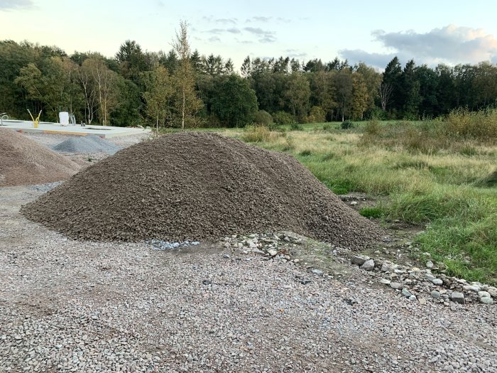 Stor hög med grovgrus (0/35) på en byggplats för användning runt husgrund.