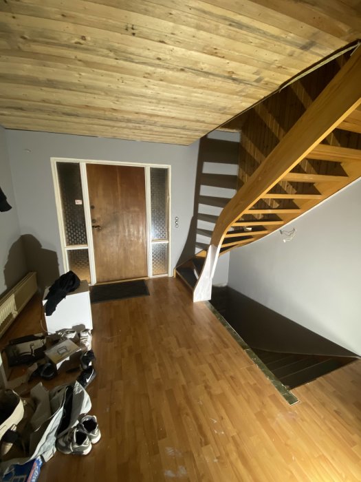 Nymålat golv i en hall med trätrappa och träpanel i taket, samt dörrar och skor på golvet.