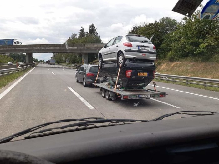 Biltransport med en bil dragen på släp och en annan bil staplad ovanpå på motorväg.