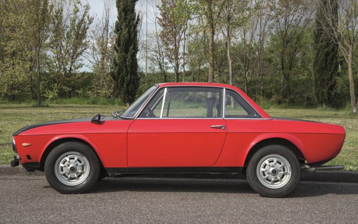 Röd Lancia Fulvia Coupe parkerad utomhus med träd i bakgrunden.