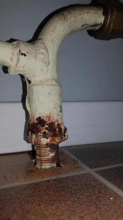 Gamla rostiga rörgängor på en koppling i värmesystem, placerad vid golvet.