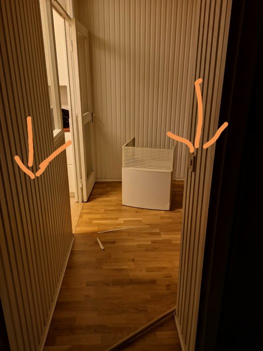 Rumsinteriör med exponerade rör och en brytardosa markerade, rivna väggar och trägolv.