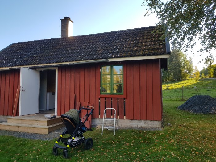 Rödmålad stuga med nyinstallerat fönster och synbara lockbrädor, barnvagn framför och en kommentar om sned grund.