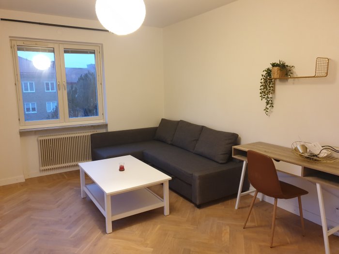 Renoverad lägenhet med nymålade väggar, trägolv, grå soffa, vitt bord och inredningsdetaljer.