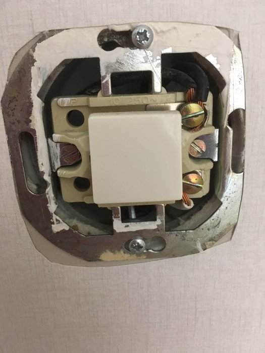En gammal strömställare monterad i väggen med två svarta kablar och en vit kabel anslutna.