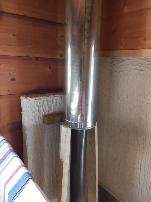 Nyinstallerat spjäll på en bastukamins skorsten i en träpanelklädd bastu.