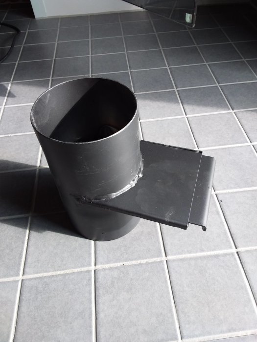 Nytt installerat spjäll på en bastupipa, placerat på ett kaklat golv.