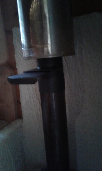 Nyligen installerat spjäll på metall bastupipa med väggen i bakgrunden.