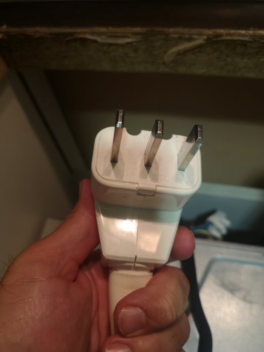 Hand håller en vit elektrisk stickkontakt med tre stift, avsedda för enfas 25A anslutning.