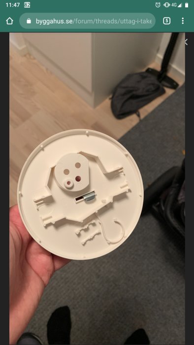 Hand håller en vit plastlock till eluttag mot en inomhusbakgrund.