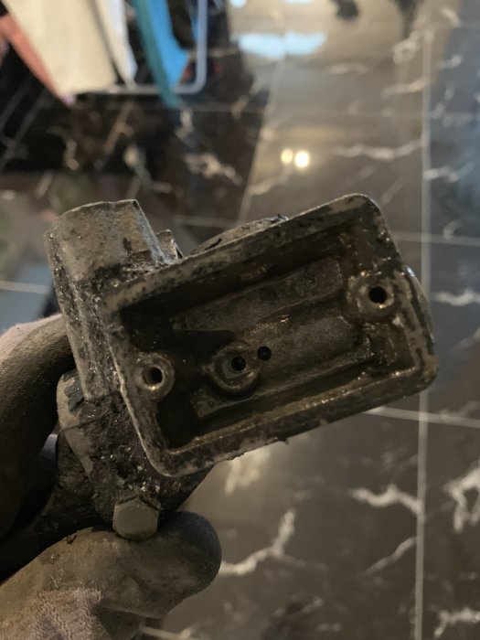 Hand håller en igentäppt ventilationsöppning täckt av damm och smuts.