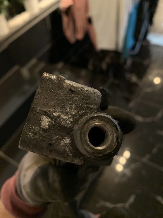Igenväxt ventil eller rörända i närbild, håller i hand mot kaklad badrumsvägg.