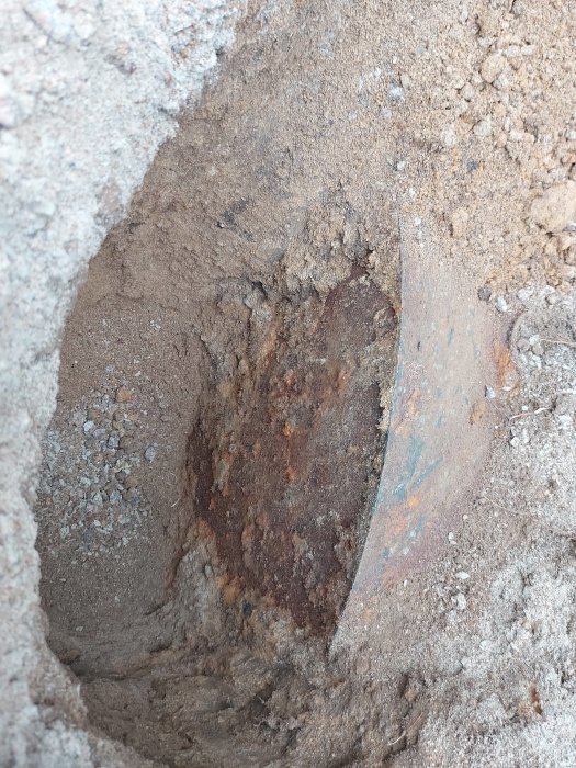 Grävning i uppfarten där man har upptäckt ett rostigt järnrör som leder in mot en vägg.