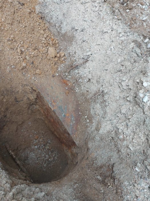 Uppgrävd uppfart med synligt rostigt järnrör som sträcker sig diagonalt ner i jorden mot en vägg.