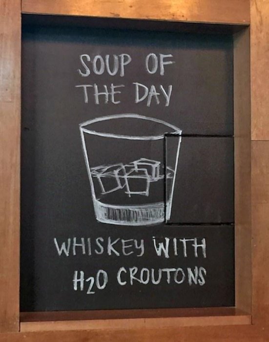 Svart tavla med texten 'SOUP OF THE DAY' och ritning av ett whiskeyglas med 'WHISKEY WITH H2O CROUTONS'.