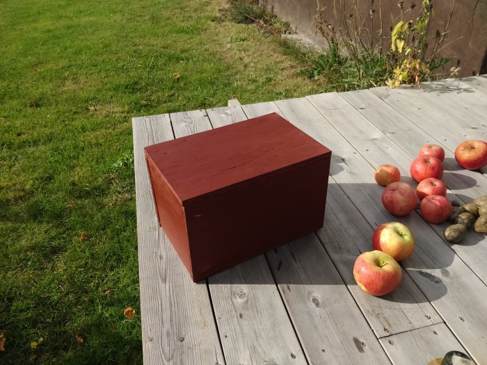 Hemsnickrad röd skovårdslåda på trätrall med äpplen och potatisar runtomkring.