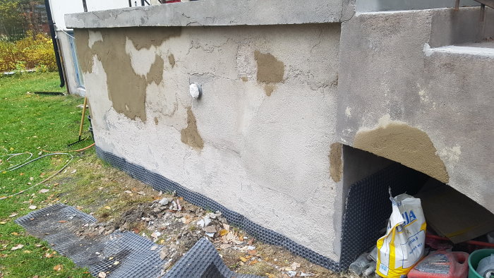 Renoveringsarbete på en husgrund med ojämnt applicerad spackel och byggmaterial på marken.