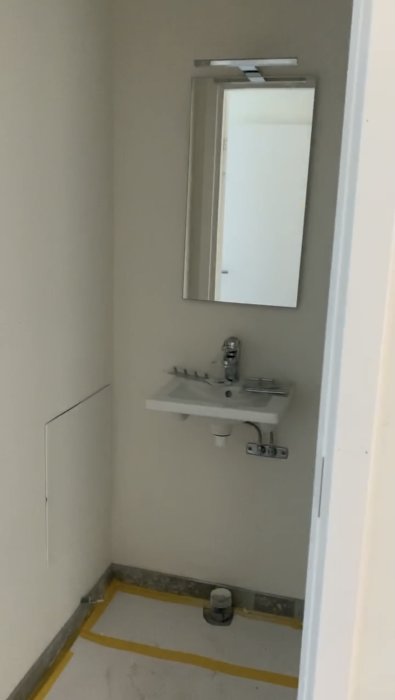 Oinredd toalett med vita väggar, handfat och spegel, förberett för renovering.