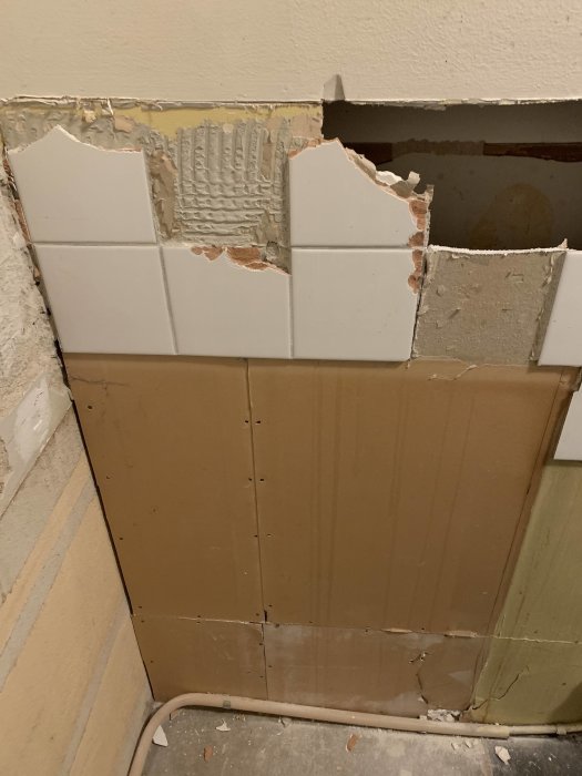 Skadad vägg med delvis borttaget kakel och synlig spricka i gipsväggen.