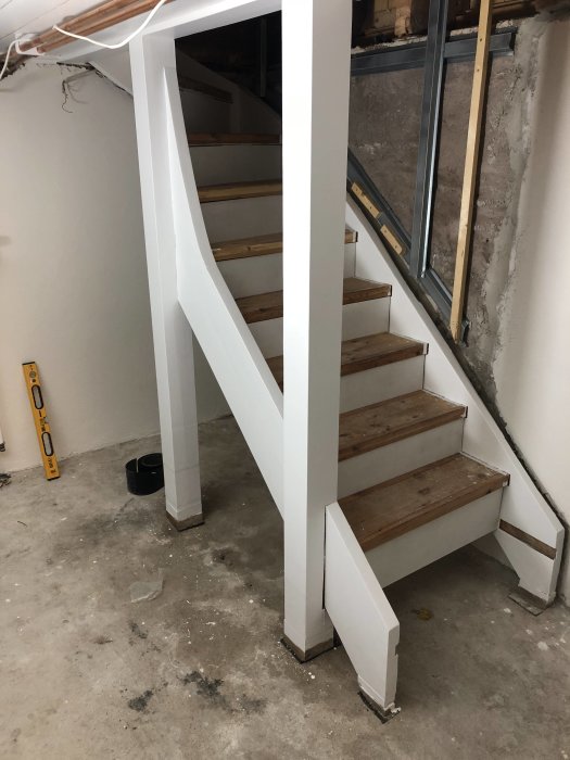 En nyligen renoverad källartrappa som omvandlats från öppen till stängd med nya vita sättsteg och trätrappsteg.