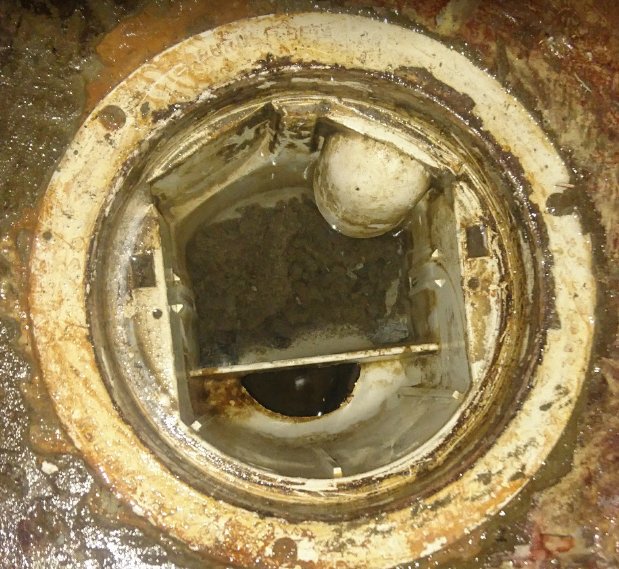 Öppen brunnslock med synlig smuts och avlagringar runt kanten och i botten.