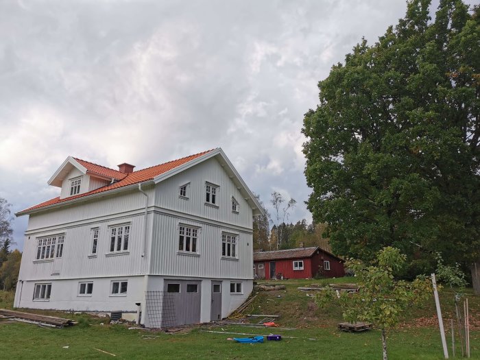 Nyrenoverad gavel på en vit tvåvåningsvilla med röda takpannor och byggmaterial framför huset.