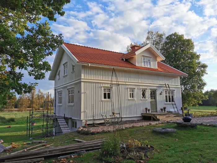 Nyrenoverad gavel på ett tvåvånings trähus i ljusgrått med rött tak och stagad byggnadsställning.