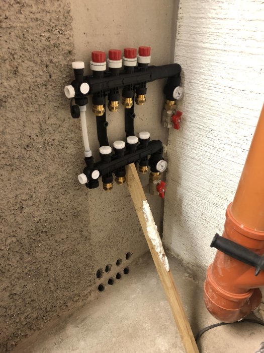 GV-fördelare monterad på betongvägg intill borrade hål och orangeröd avloppsrör i en källare.