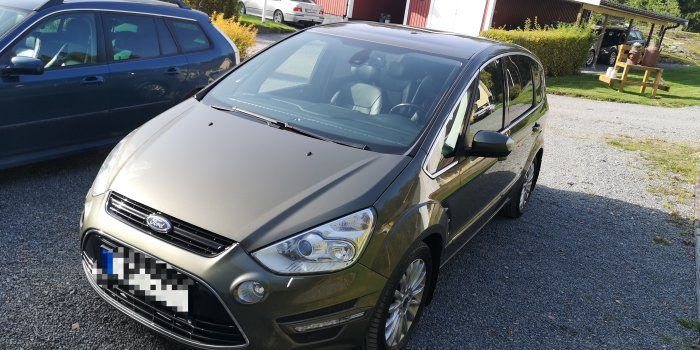 En metallicgrå Ford S-Max från 2012 parkerad utomhus med tydliga linjer och i gott skick, omtyckt av familjen efter provkörningen.