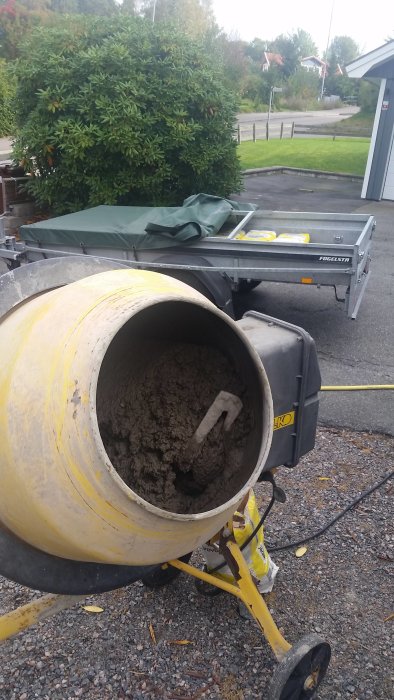 Betongblandare med rester av betong framför släpvagn på uppfart.