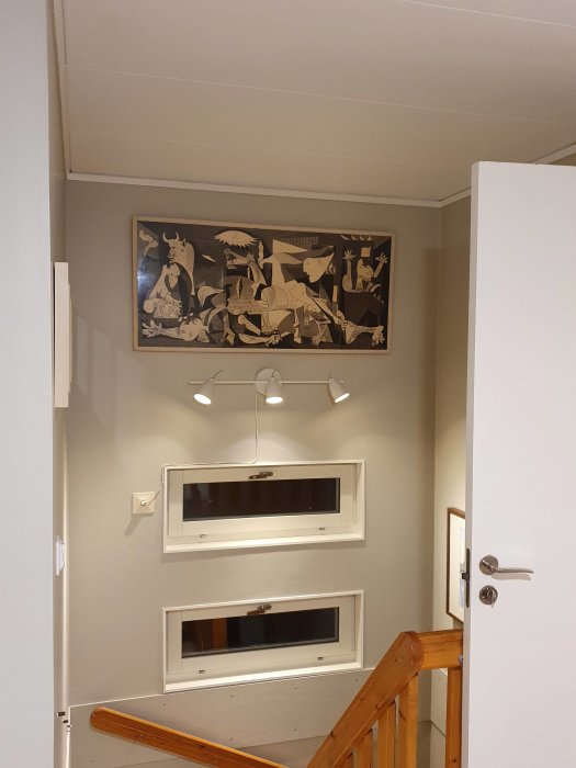 Picasso-tavla hängd ovanför trappan, med spotlight och dekorativa fönster ovanför.